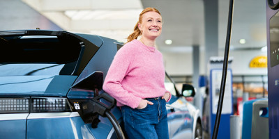 Vrouw met roze trui staat naast auto dat laadt bij Q8 electric