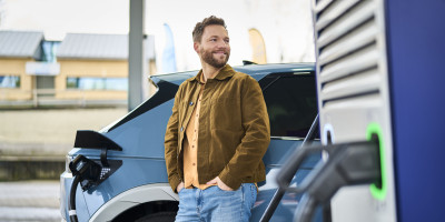 Man staat naast zijn elektrische wagen dat word geladen bij Q8 electric