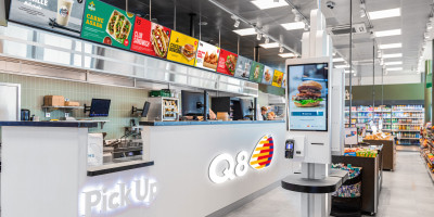 Zelfbedieningskiosk en afhaalbalie in Q8-tankstation met broodjes, burgers en snacks.